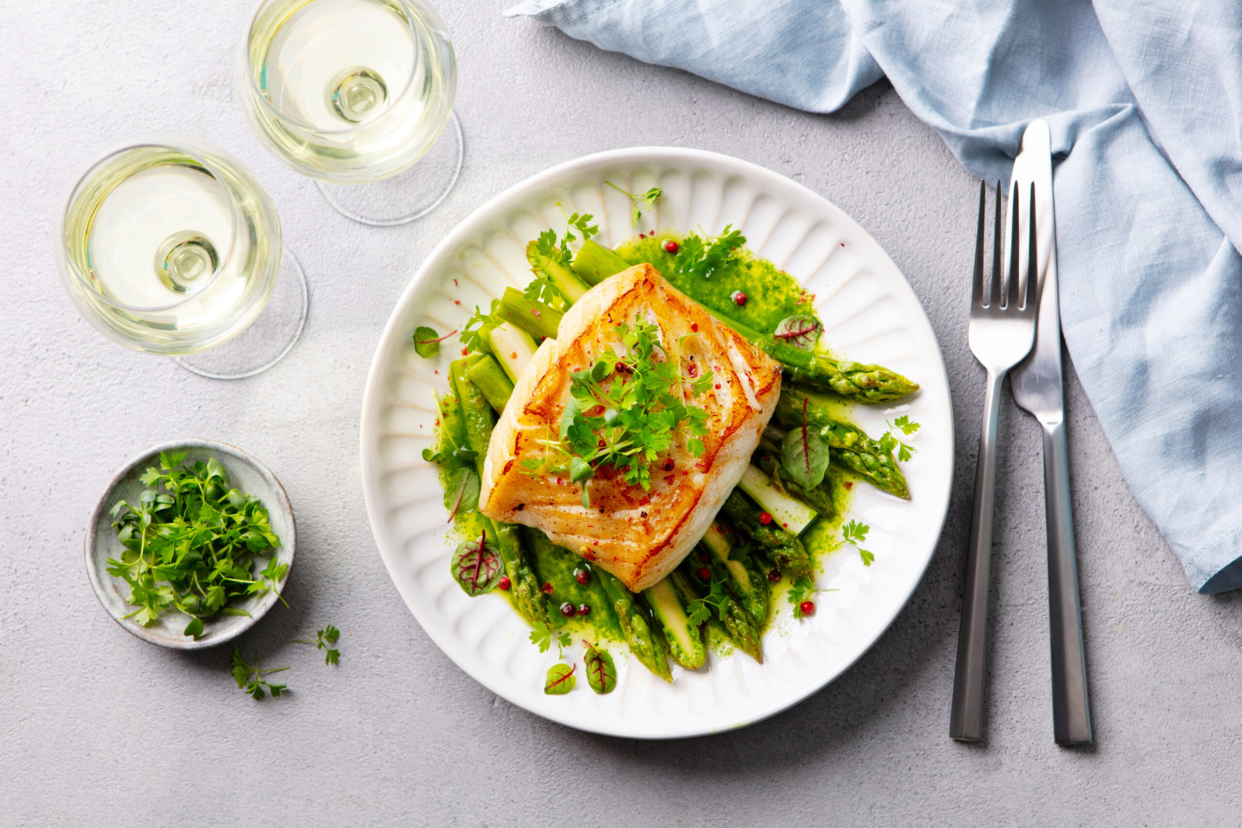 Roasted cod, codfish with asparagus and on plate and white wine. Grey background. Close up.